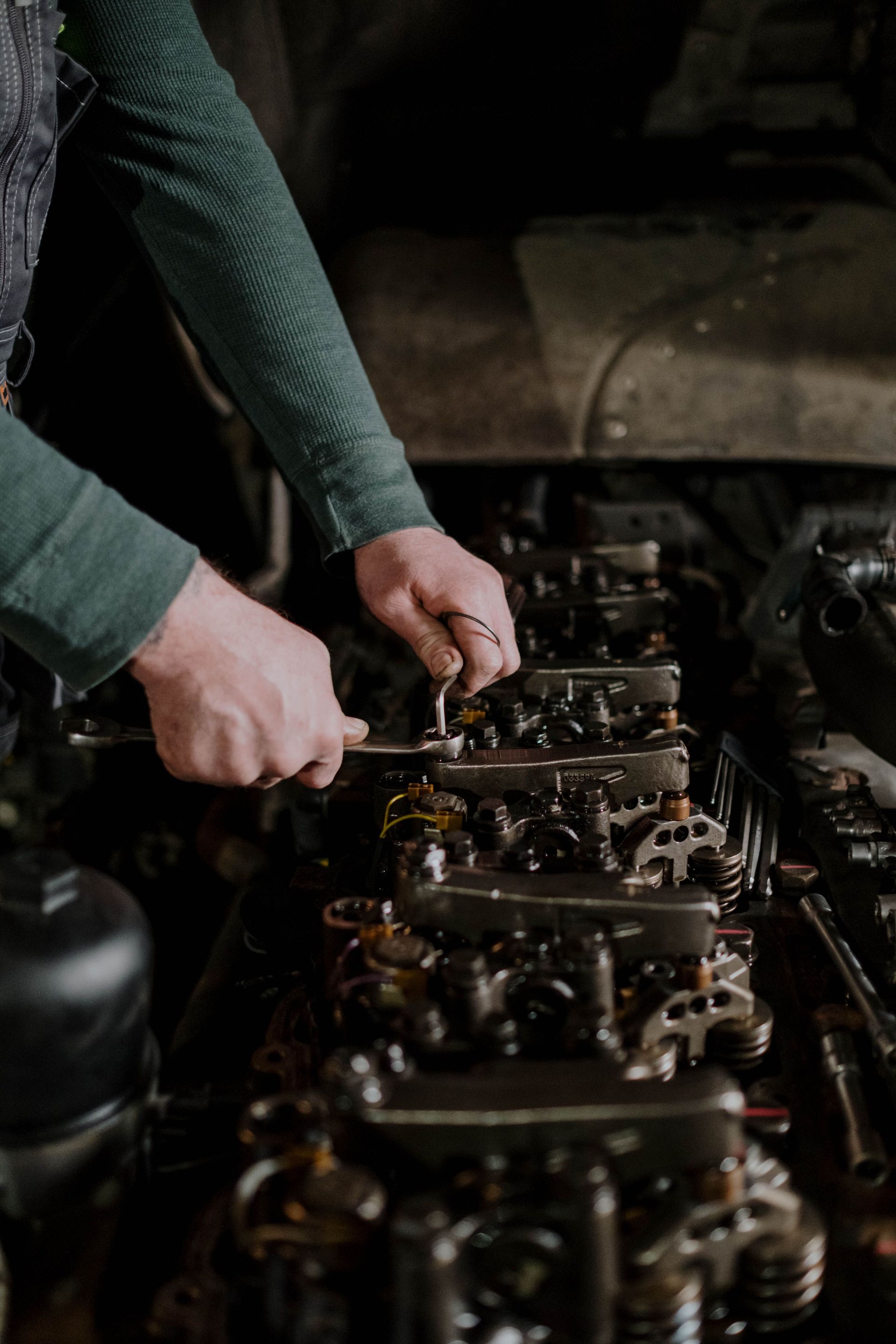 Close-up of a mechanic's hands using tools to repair an engine. Indoor setting.